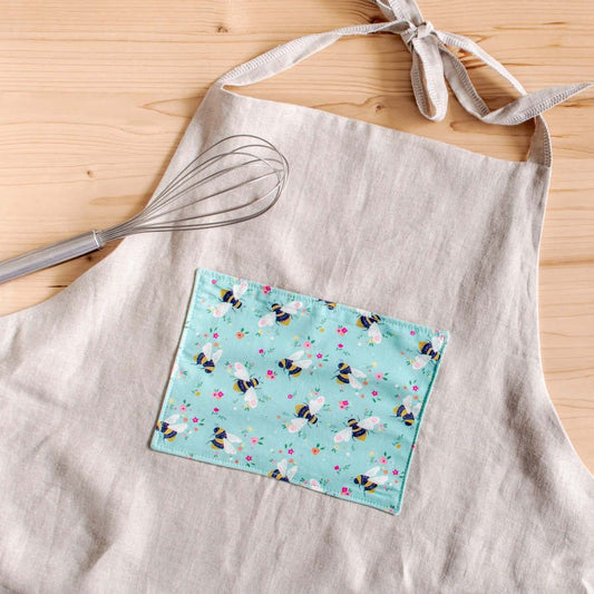 Light grey apron  with pocket in the front made of Blue organic cotton poplin with black and yellow bees and colourful flowers